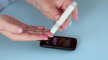 Diyabet izleme konsepti. Kan şekerini ölçmek için glukometre kullanan bir kadın. Evde kan şekeri kontrolü. Glikoz testi. Açık mavi arkaplan, 4k