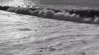 Beyaz köpüklü büyük güç dalgaları. Deniz fırtınalı. Büyük deniz dalgalarıyla kıyı şeridi. Köpükle sörf yapmak. Gün batımında güzel deniz manzarası, ağır çekimde köpüklü dalgalar.
