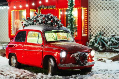 Çatıda Noel ağacı olan kırmızı bir araba kırmızı bir dükkanın arka planına karşı. Yeni yıl süslemeleri ve sokakta kar olan eski kırmızı bir araba. Aile fotoğrafları için arabası olan bir noel fotoğrafı bölgesi.