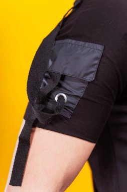Sarı arkaplandaki siyah tişörtün ayrıntıları. Sade renkli bir arka planda bir yaz tişörtünün makro fotoğrafı. Bir fotoğraf stüdyosunda yaz kıyafetlerinin fotoğraf çekimi.