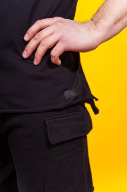 Sarı arkaplandaki siyah tişörtün ayrıntıları. Sade renkli bir arka planda bir yaz tişörtünün makro fotoğrafı. Bir fotoğraf stüdyosunda yaz kıyafetlerinin fotoğraf çekimi.