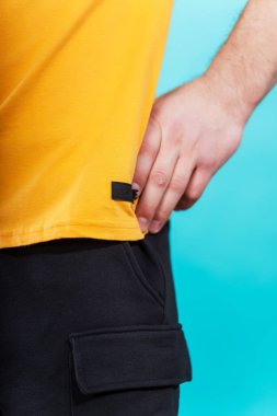 Sarı arkaplandaki siyah tişörtün ayrıntıları. Sade renkli bir arka planda bir yaz tişörtünün makro fotoğrafı. Bir fotoğraf stüdyosunda yaz kıyafetlerinin fotoğraf çekimi.