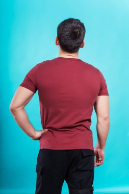Mavi arka planda, bordo tişörtlü bir adam. Burgundy tişörtlü, sade renkli bir arka planı olan bir adamın arkası. Bir fotoğraf stüdyosunda yaz kıyafetlerinin fotoğraf çekimi.