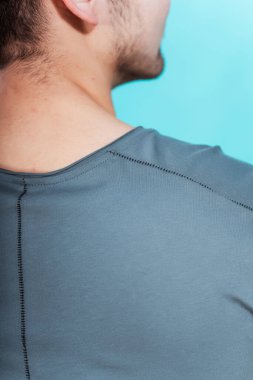Mavi arka planda gri tişörtlü adam. Gri tişörtlü, sade bir arka planı olan bir adamın arkası. Bir fotoğraf stüdyosunda yaz kıyafetlerinin fotoğraf çekimi.