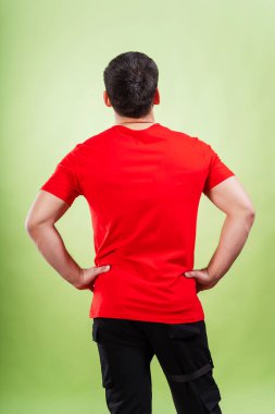 Yeşil arka planda kırmızı tişörtlü adam. Beyaz tişörtlü, sade bir arka planı olan bir adamın arkası. Bir fotoğraf stüdyosunda yaz kıyafetlerinin fotoğraf çekimi.