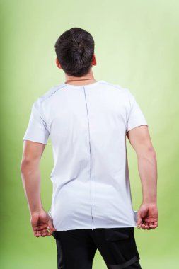 Yeşil arka planda beyaz tişörtlü bir adam. Beyaz tişörtlü, sade bir arka planı olan bir adamın arkası. Bir fotoğraf stüdyosunda yaz kıyafetlerinin fotoğraf çekimi.