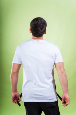 Yeşil arka planda beyaz tişörtlü bir adam. Beyaz tişörtlü, sade bir arka planı olan bir adamın arkası. Bir fotoğraf stüdyosunda yaz kıyafetlerinin fotoğraf çekimi.