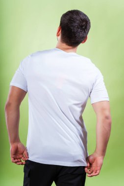 Yeşil arka planda beyaz tişörtlü bir adam. Beyaz tişörtlü, sade bir arka planı olan bir adamın arkası. Bir fotoğraf stüdyosunda yaz kıyafetlerinin fotoğraf çekimi.