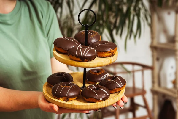 chocolate donuts on a wooden tray in the girl\'s hands. flour donuts with chocolate icing on a wooden plate. colorful pastries for guests