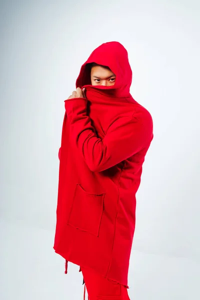 photo shoot of a Korean guy on a white background. A Korean model in a fashionable cape with a half-covered face. photo shoot of youth clothes with a model in a photo studio