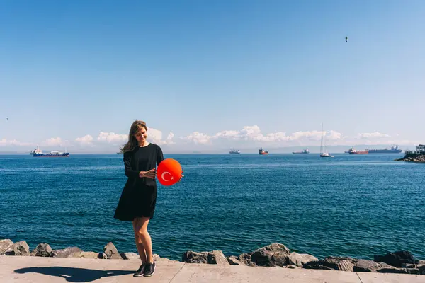 A girl in a black dress with a red balloon in her hand on the Istanbul pier. Russian girl with a Turkish balloon on the background of the sea. a single woman in Turkey