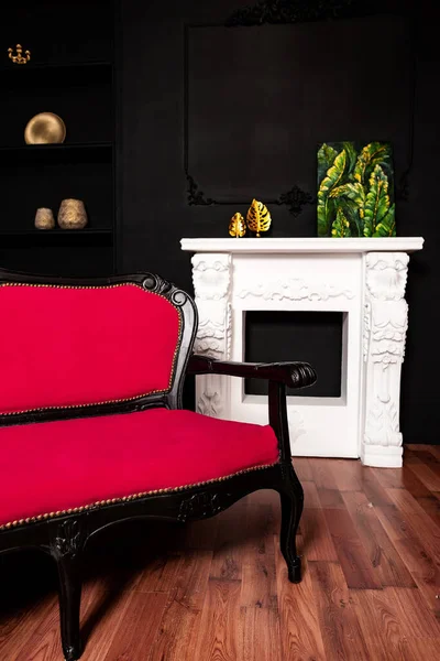 a black and red sofa against a black wall with shelves and a white fireplace. wedding photo zone in Gothic style in a photo studio. classic room in black in the house