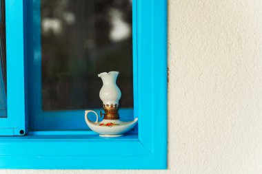 Pencerenin pervazında duran bir lambanın bulunduğu mavi bir pencere var. Atmosfere sıcak bir ortam katıyor.