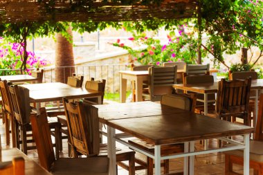 Çok güzel hazırlanmış ahşap bir güvertede çeşitli şık masalar ve açık hava eğlencesi için zarif sandalyeler var.