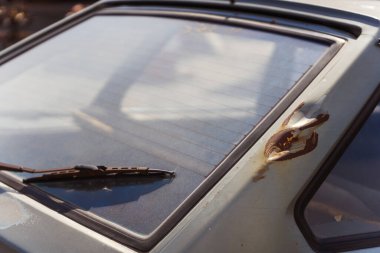 Bu, eski, paslı bir arabanın ayrıntılı bir yakın plan görüntüsü. Yan tarafında sarı bir ışık var ve yıpranmış görünümünü gösteriyor.