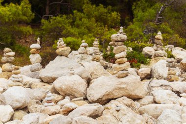 Ön planda, birbiri üzerine dikkatlice istiflenmiş etkileyici bir taş yığını var. Arka planda ağaçlar görülebiliyor.