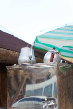 Bir konteynırın üstüne iki çaydanlık yerleştirilir. Konteynır büyük bir şemsiye altında yer alır. Gölge ve koruma sağlar.