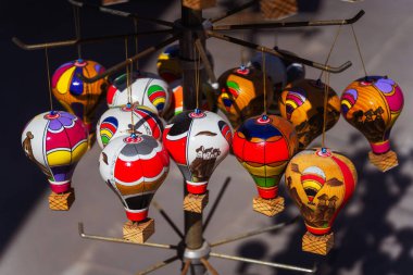 Renkli sıcak hava balonlarının canlı bir çeşidi sanatsal olarak sergilenmiş, güçlü bir direğe nazikçe asılmış, neşeli bir ortam yaratıyor.