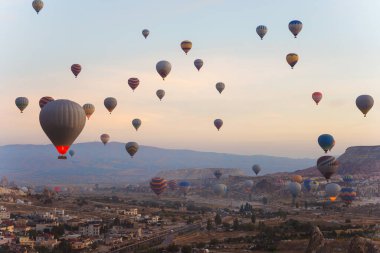 Canlı ve renkli bir grup sıcak hava balonu açık gökyüzüne yükseliyor, aşağıdaki hareketli şehrin üzerinde görkemli bir şekilde uçuyor.