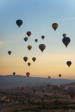 Canlı ve renkli bir grup sıcak hava balonu açık gökyüzüne yükseliyor, aşağıdaki hareketli şehrin üzerinde görkemli bir şekilde uçuyor.