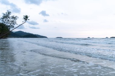 Alacakaranlıkta sakin ve sakin bir deniz manzarası, yumuşak dalgalar ve güzel manzaralı bir arka plan.