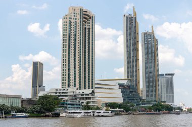 Parlak bir gökyüzünün altında sakin bir nehir boyunca uzanan etkileyici yüksek binaları gösteren nefes kesici modern bir siluet.