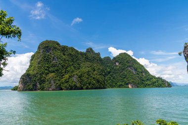 Turkuvaz suları ve açık mavi gökyüzü ile çevrili yemyeşil bir adanın çarpıcı manzarasına bakın.