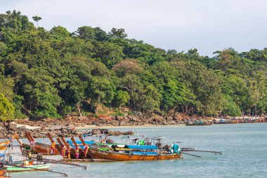 Kayalık bir adanın yakınındaki kristal berrak turkuaz sularda zarifçe gezinen bir teknenin huzurlu ve huzurlu görüntüsü.