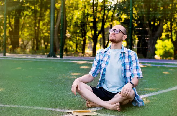 A young man is resting in the park. A male businessman is resting in nature. Happy student in the park. A man reads a book on the grass. Relaxation and rest of a man in nature