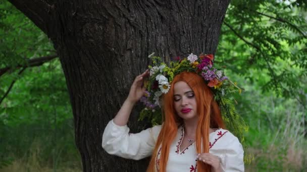 美丽的女孩 红头发 头戴花冠 头戴白色和红色绣花民族服装 站在树旁 童话人物 森林精神 Mavka — 图库视频影像