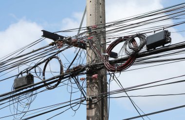 Bulut ve mavi gökyüzü arkaplanlı sokak direğinde dağınık elektrik kabloları ve kablolar
