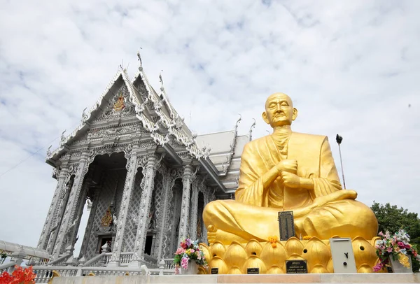 Golden colored of Somdet Budhacariya (Toh Brahmaransi) statue with silver church in background at Wat Don Yai in Pathum Thani province, Thailand.