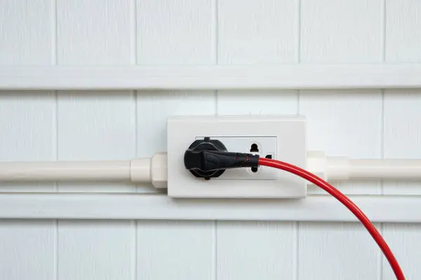 An electric plug with a red cable in the socket.