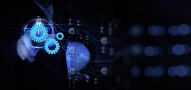 Mavi dişlileri ve dijital güvenlik simgelerini gösteren, mühendisliği, otomasyonu ve teknolojiyi simgeleyen sanal bir arayüzle etkileşime geçen bir iş adamının gelecekteki görüntüsü..