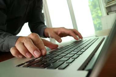 Parlak, modern bir ofiste, ahşap bir masada dizüstü bilgisayarda yazı yazan bir iş adamının ellerini kapatın. Görüntü mesleki çalışma, iş iletişimi, kurumsal ortam temalarını iletir,