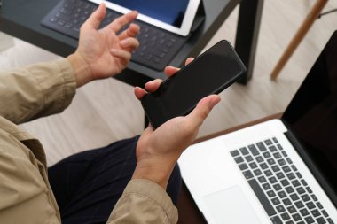  Bir yanda akıllı telefon tutan bir adamın, diğeriyle iş görüşmesi sırasında el kol hareketi yaparken yakın plan görüntüsü. Bir dizüstü bilgisayar ve tablet, modern, teknoloji meraklısı bir çalışma alanını işaret ediyor..