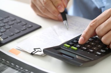 Close up of a person using calculator and pen to calculate expenses, taxes, or budget on desk with receipts, keyboard, and financial papers. Perfect for business, accounting, or finance concepts.