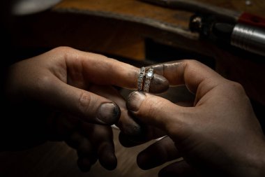 Closeup of a diamond wedding ring and dirty jeweller hands holding it clipart