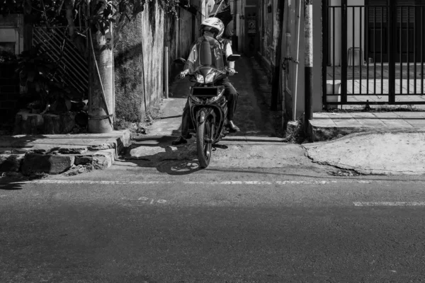 Bu motosikletçi dar bir sokaktan yeni çıkmıştı, ve ana yola girmek üzereydi, belki de işe gidiyordu. Bu, Endonezya 'nın Yogyakarta kentindeki sokak fotoğrafçılığının sonucudur..