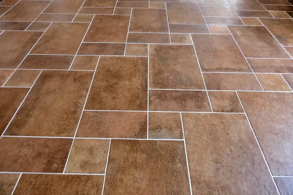 新しく敷設されたイタリアのテラコッタの茶色の床のタイルは灰色の溝で仕上げ ストックフォト