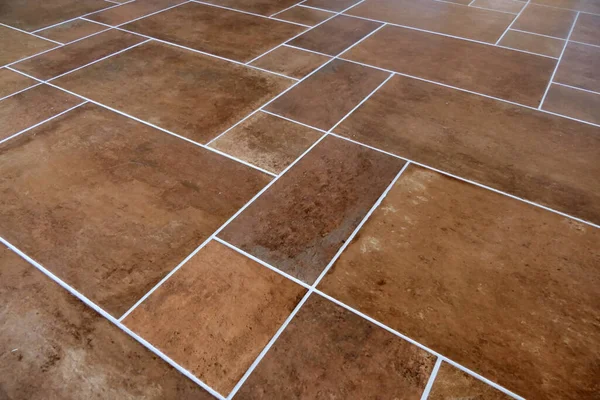 新しく敷設されたイタリアのテラコッタの茶色の床のタイルは灰色の溝で仕上げ ストック写真