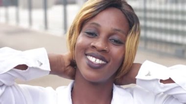 Beyaz gömlekli kız saçını düzeltiyor, gülümsüyor.