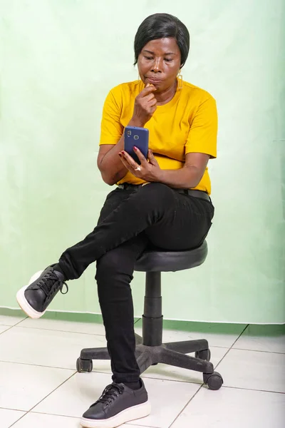 Beautiful Mature Woman Yellow Shirt Sitting Green Background Looking Cellphone — Stock Photo, Image