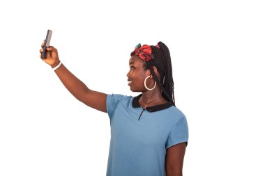 Beyaz bir arka planda duran genç bir kız akıllı bir telefonla gülerken fotoğrafını çekiyor..