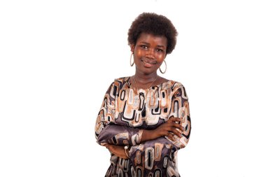 Beyaz bir arka planda afro saçlı güzel bir genç kız kollarını kavuşturarak kameraya bakıp gülümsüyor..