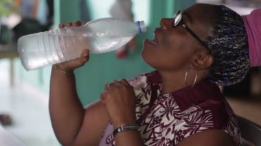 Olgun bir kadın oturma odasında oturmuş şişede su içiyor.