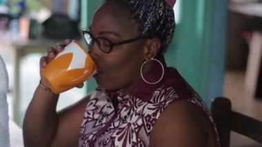 Olgun bir kadın oturma odasında oturmuş bir kasede su içiyor ve gülümsüyor..