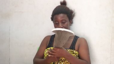 Güzel bir kadın evde oturmuş bir vantilatörle üflüyor