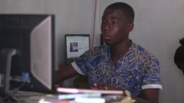 Genç adam bir odada oturup dizüstü bilgisayarla çalışıyor.