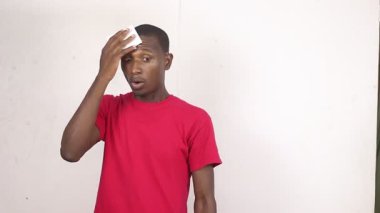 Beyaz arka planda duran kırmızı tişörtlü yakışıklı bir adam yüzünü sildikten sonra gülümseyen bir mendil gösteriyor..